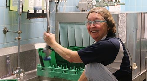 A smiling school cafeteria worker at the kitchen sink.