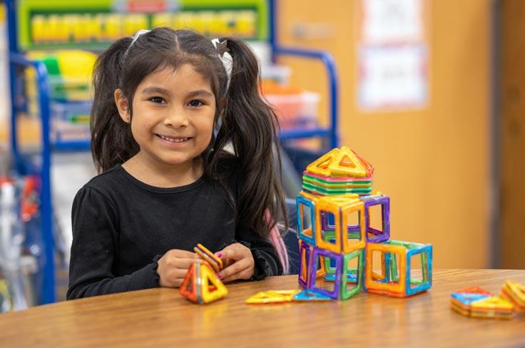 A smiling student working with connecting building manipulatives.