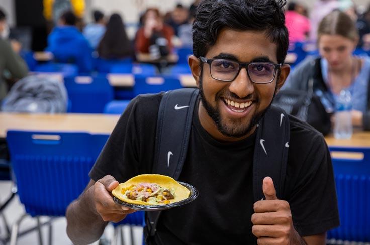 A high school student giving a happy "thumbs up" while showing off his taco plate.