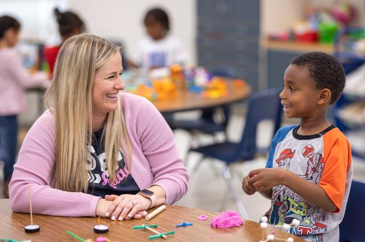 A teacher and student smiling as they work with manipulatives and playdoh at a table.