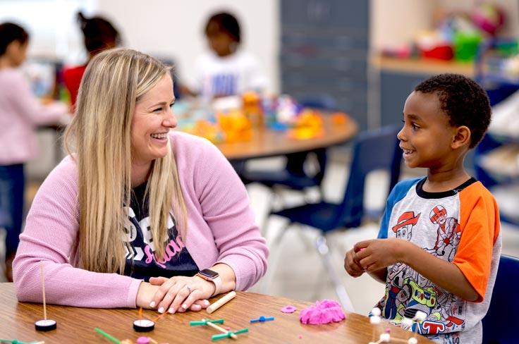 A teacher and student smiling as they work with manipulatives and playdoh at a table.