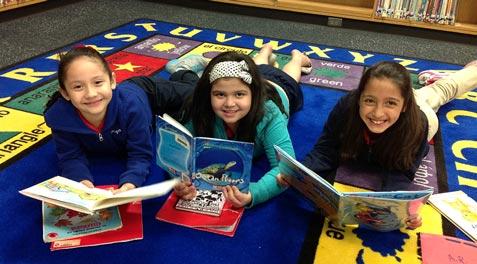 Three girls feeling comfy on a rug in a library with their books.