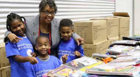 Linda Griffin posing with several kids next to the school supplies for the NAACP's B2S Rally Drive.