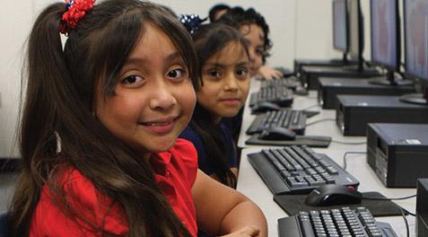 Young students smiling at the camera while in the computer lab.
