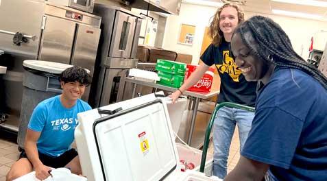 Three students helping pack ice chests with drinks.