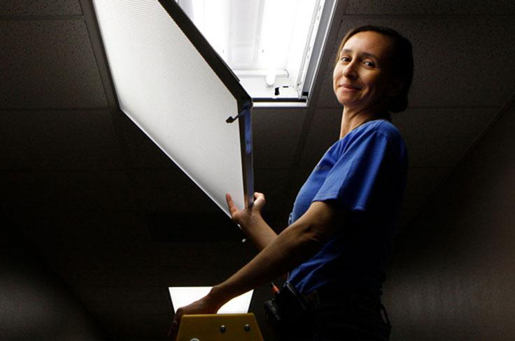 A GISD custodian changing out a ceiling light, smiling for the camera.