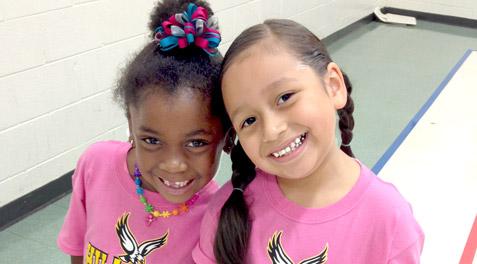 Two kindergarten girls posing together in matching pink shirts.