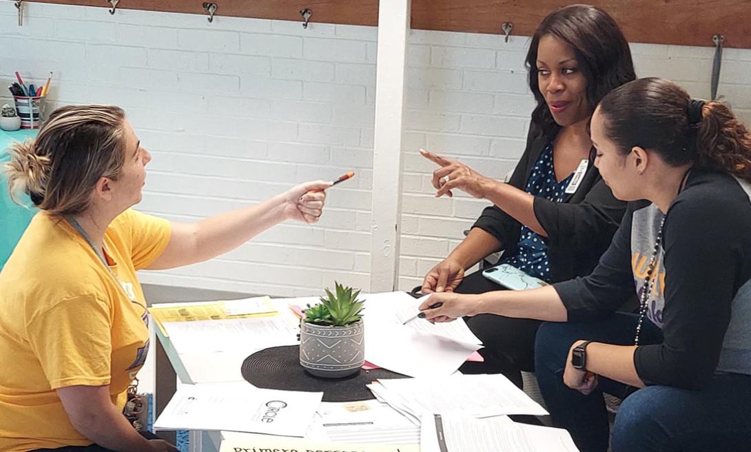 Two teachers and one central office staff member actively gesturing while planning together at a Pre-K classroom table.