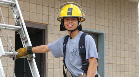A student in the Garland ISD Firefighting program posing in uniform on a ladder at our practice building.