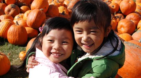 Two little girls in jackets hugging each other at a pumpkin patch.