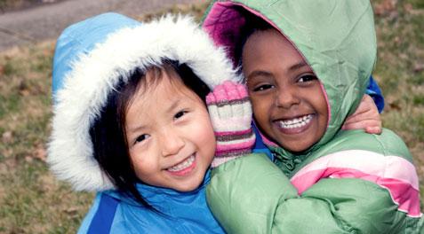 Two little girls in coats and mittens smiling together outside.