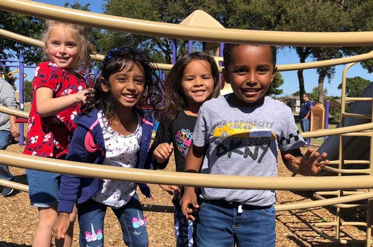 A diverse group of smiling young children on playground equipment