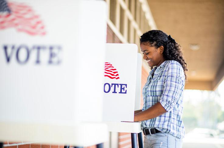 An African-American woman smiling while casting a vote at a voting booth.