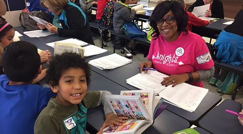A woman and student smile while working alongside many tutors and their students.