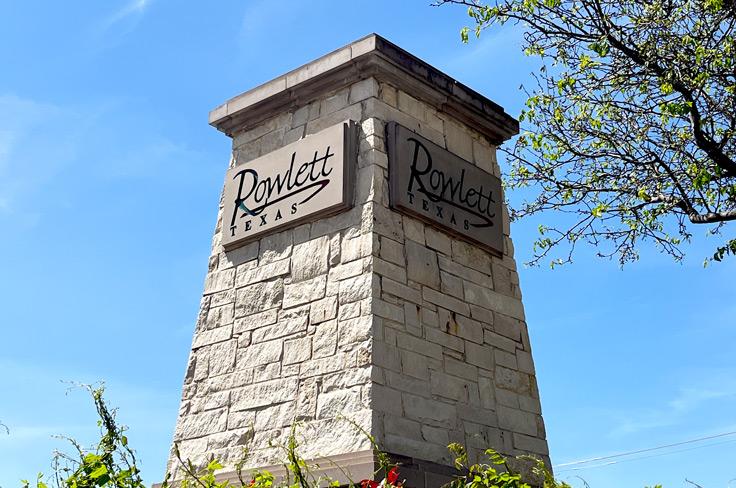 A white stone short polygon tower, featuring Rowlett's city logo on all four sides.