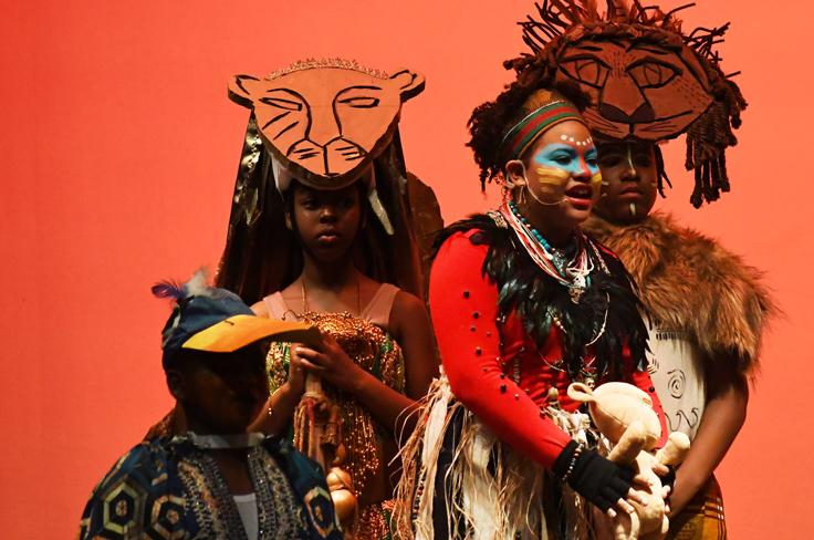 Elementary students perform "The Lion King" as part of the Vial theatre program. Students are dressed in tribal wear, with animal masks, organic accessories like feathers, and facepaint.