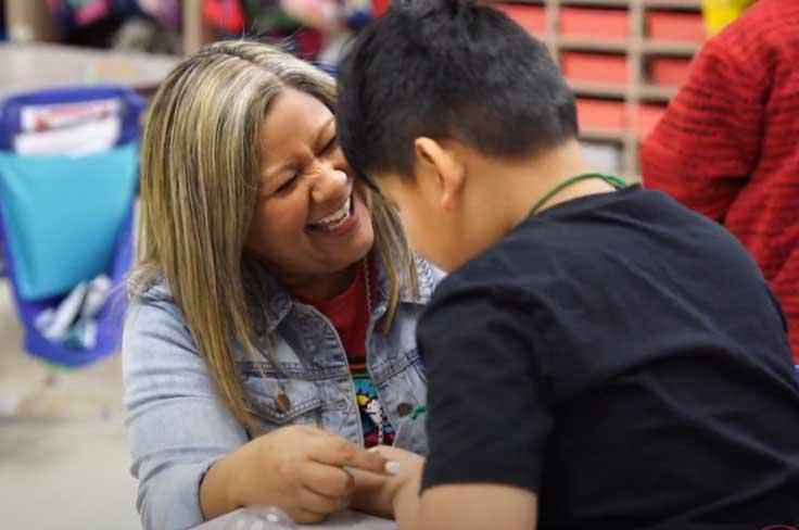 Laughing teacher leaning in to help student