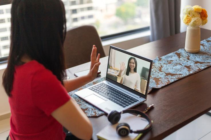 A student on a video call waving to her therapist while sitting at her kitchen table.