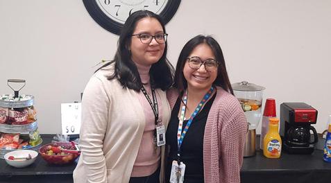 Two substitutes smiling in front of a table filled with snacks and drinks to honor substitutes.