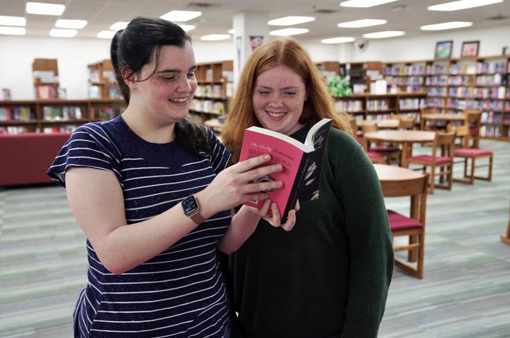 A student and student author reading their book in the library.