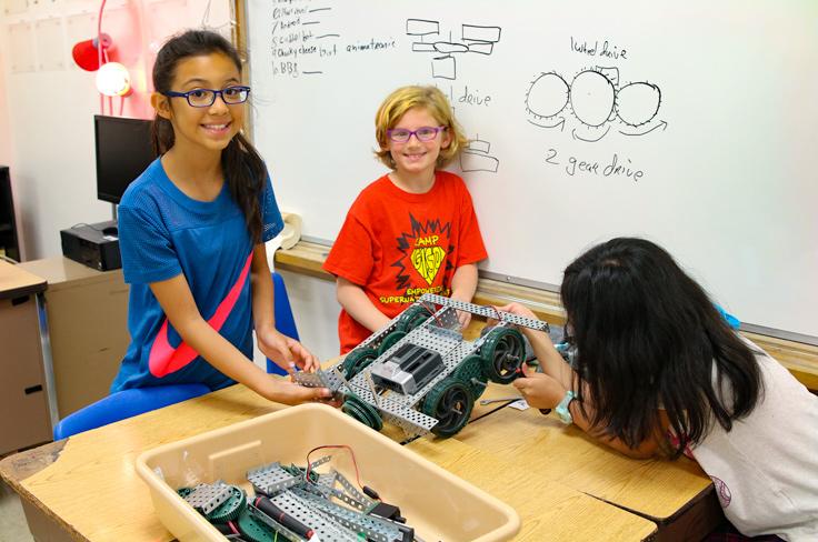 Students at school summer camp smiling for a photo while working together to assemble a robot.