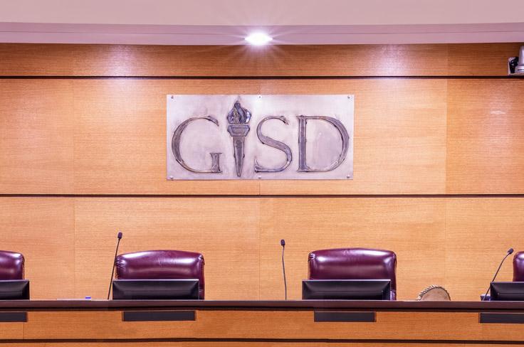 The Garland ISD Board room, featuring leather chairs behind a long podium and the handcrafted metal "GISD" sign.