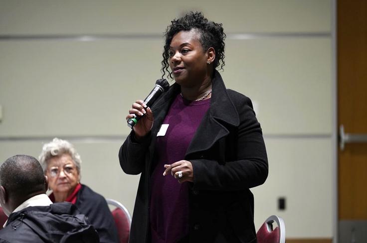 An African-American woman speaking to the community during a committee meeting.