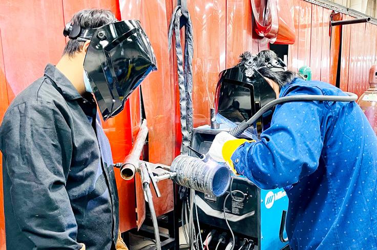 Two students in welding gear burning metal for a project.