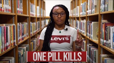 A LCHS Sophomore holding one of her fingers up in a "1" with the banner "One Pill Kills".