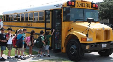 Young students with backpacks lined up to board a bus.