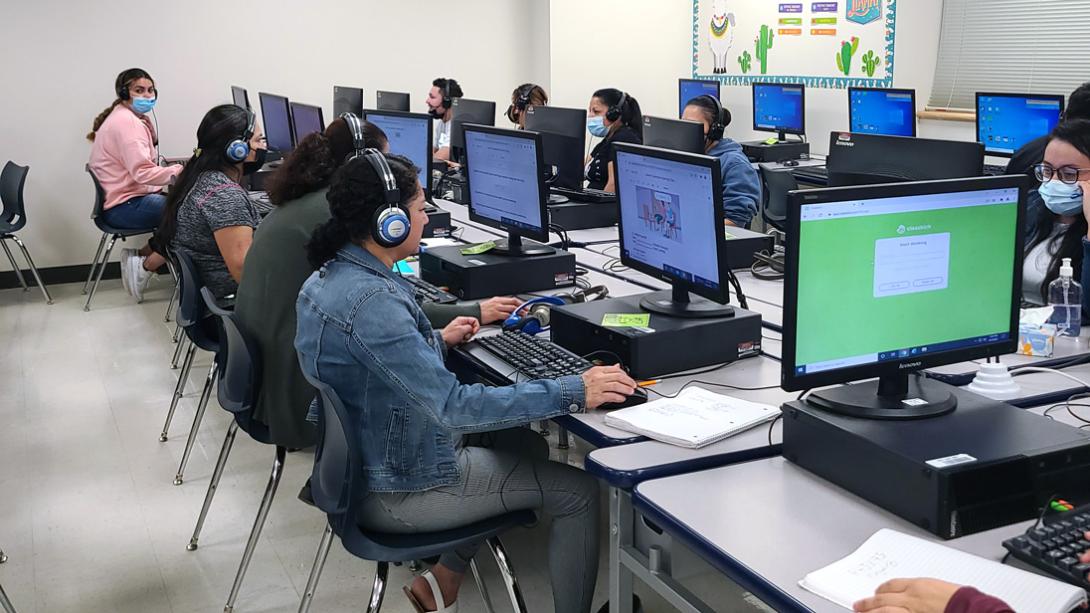 A group of adults working on language projects in a school computer lab.