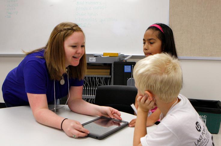 A youthful teacher helping two elementary students with an iPad.