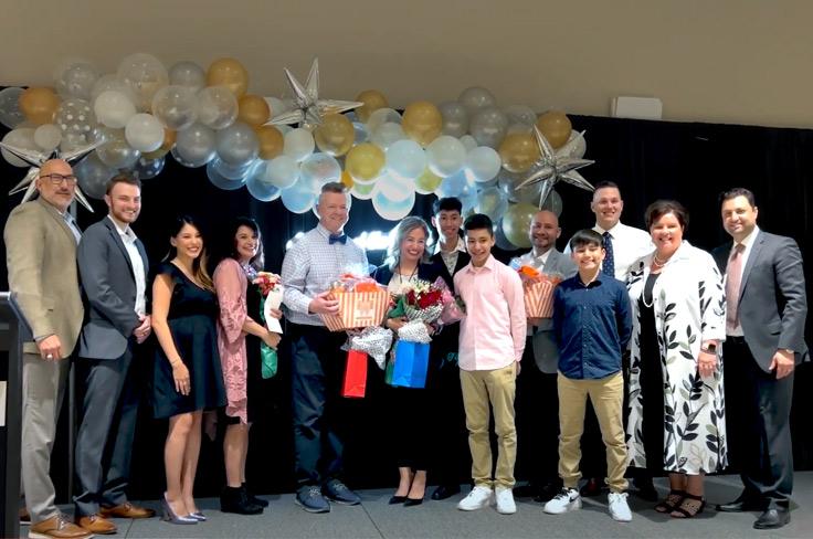 The 2022-23 Teachers of the Year standing on a podium posing for a photo with their families as well as the Superintendent, GEF, and other staff. Behind them is a decorative balloon garland and neon "teacher of the year" sign.