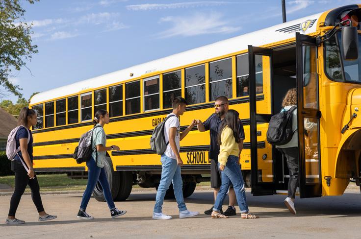 A bus driver greets students with fist bumps as they board the bus.