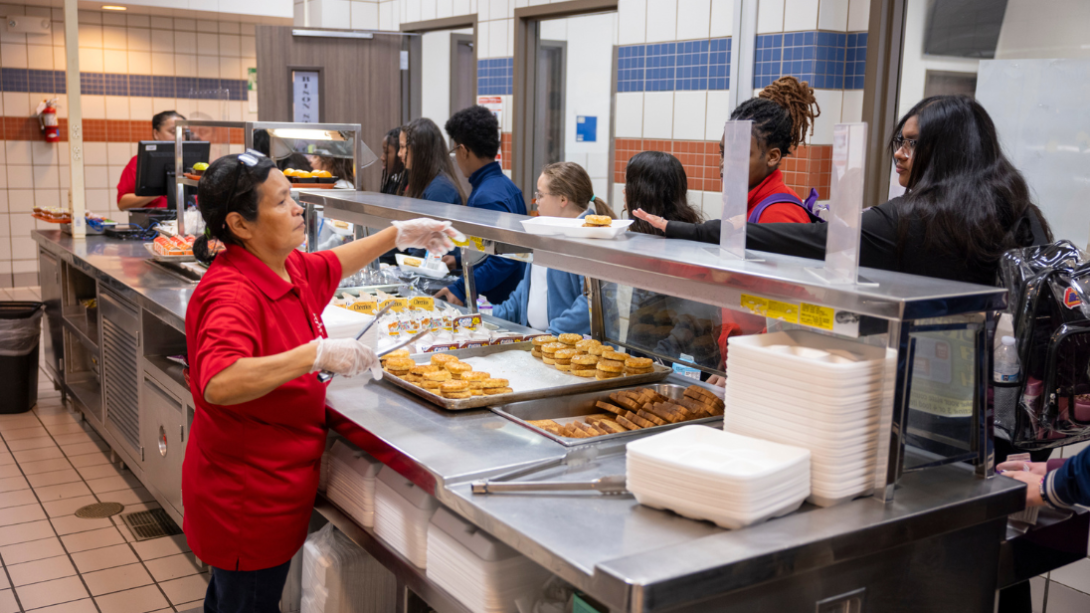 A group of students in line to receive breakfast from a cafeteria worker