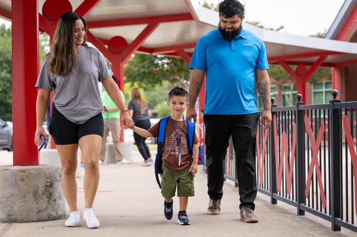 A family holding hands, walking with their young student on the first day of school.