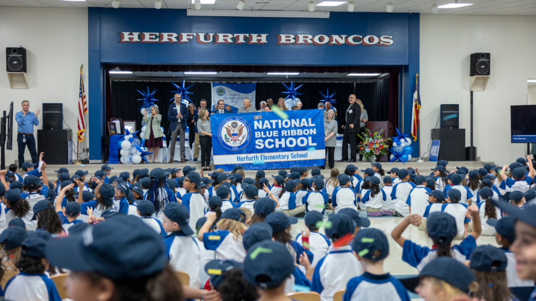 crowd of students and staff stand cheering as banner is displayed