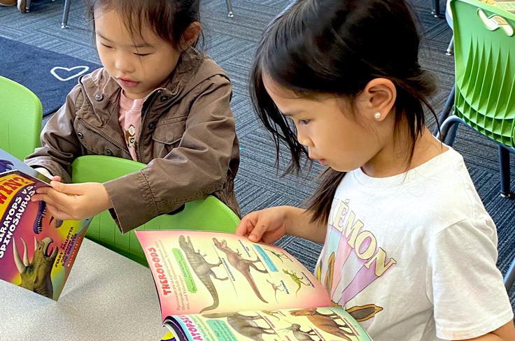 Two girls in elementary reading dinosaur books.