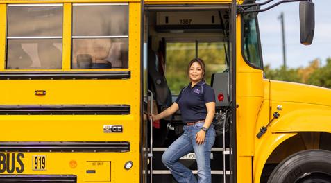 A bus driver wearing a GISD Transportation polo poses on the steps of her bus.