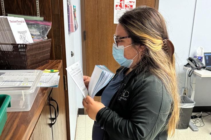 One of the Student Services Clinic nurses preparing paperwork by a bookshelf.