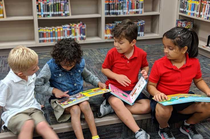 Young students sitting on the floor in the library holding books.