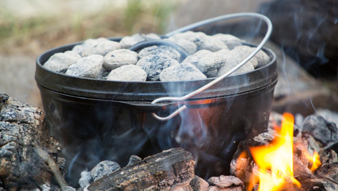 A Dutch oven with coals cooking over an outdoor fire.