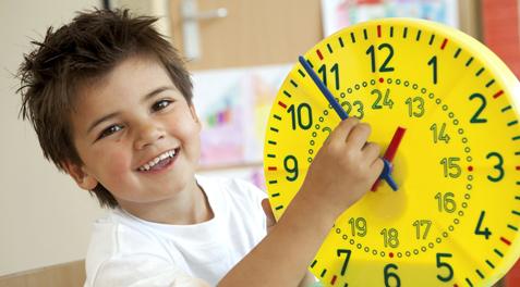 A student smiles while holding a large, yellow time-teaching clock.