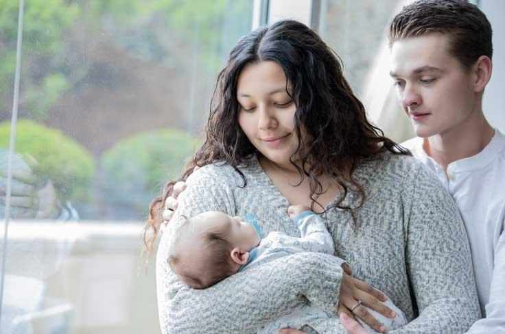 Teenage girl holding a baby while teenage boy stands close with his arm around her