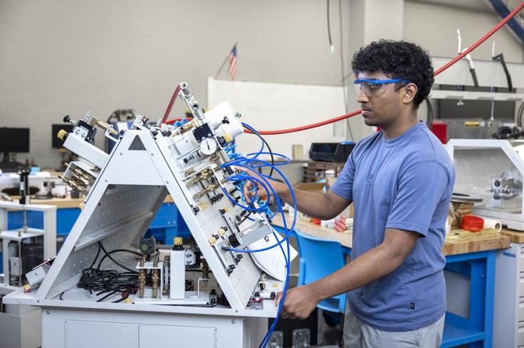 A student in safety glasses works on a pressurized pump board, wires going everywhere.