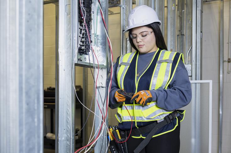 A girl works on cutting electrical wires inside a housing frame, wearing full protective gear.