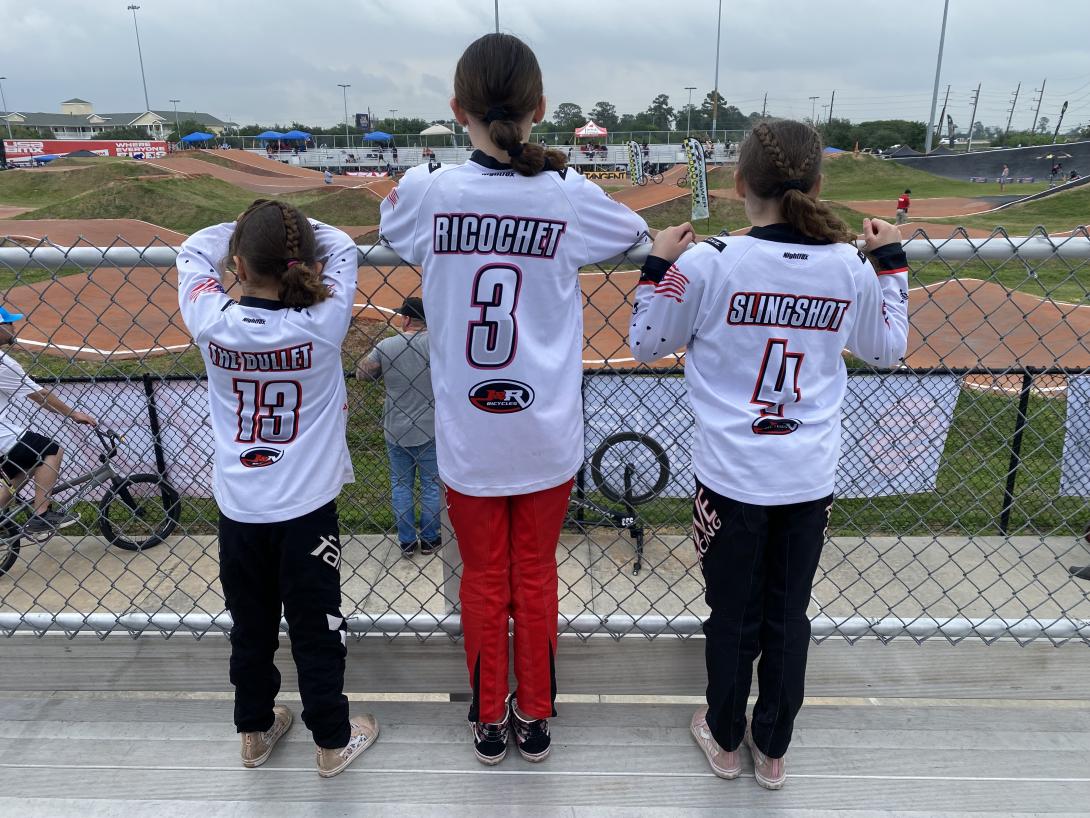 bmx sisters stand facing away in their jerseys