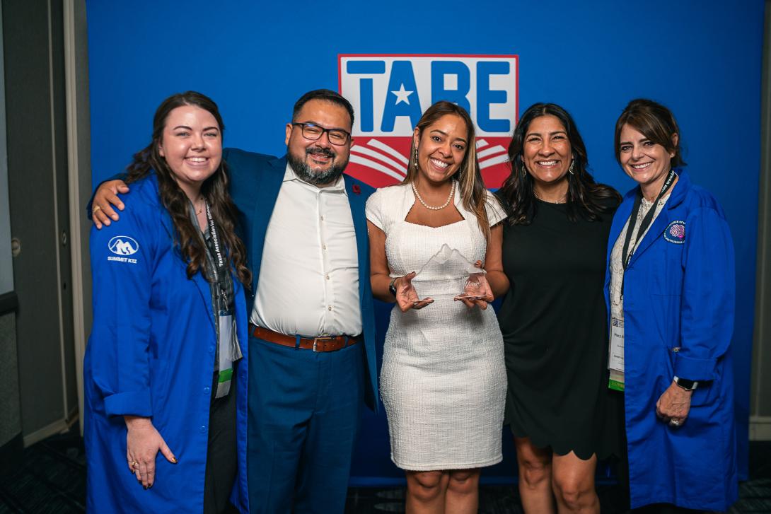 four women and one man stand with the woman in the middle holding an award