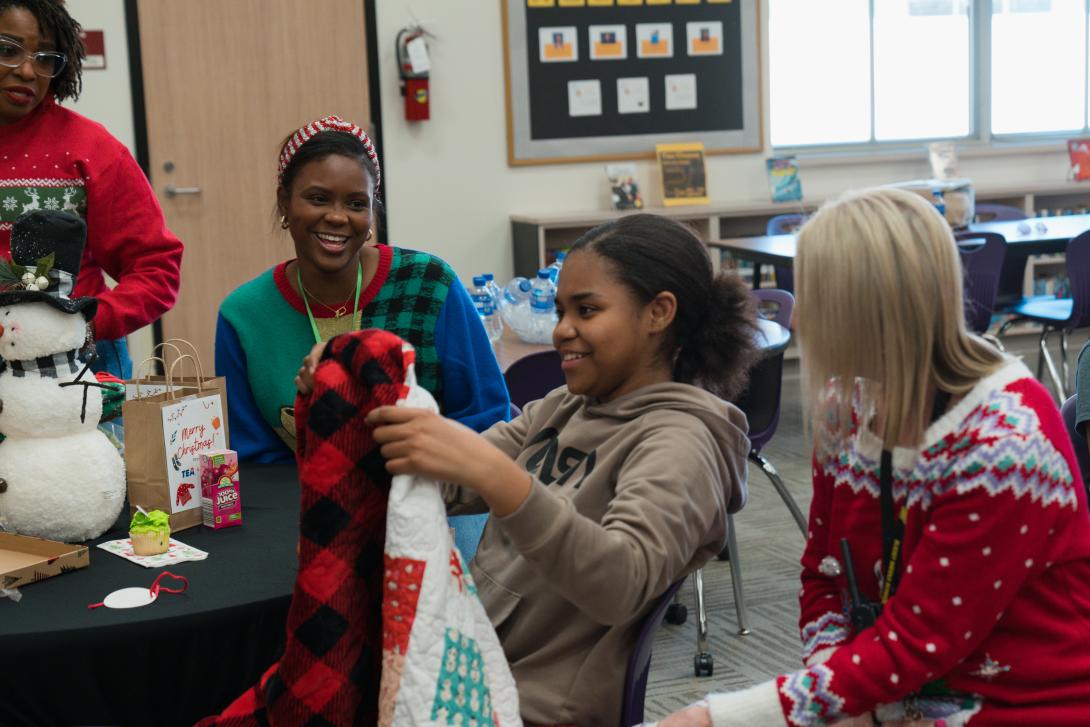 student opens gift with three adults nearby