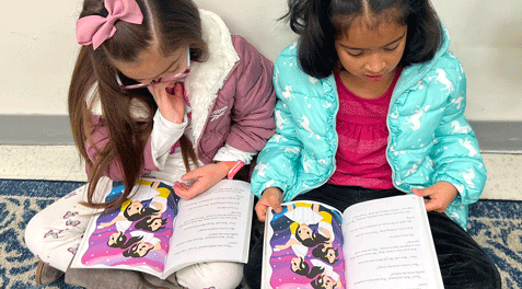 Two young girls reading a princess book on a rug in class.